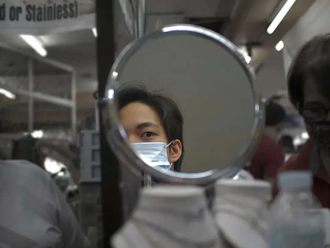 Young man examining his facial features in mirror with thoughtful expression, demonstrating self-assessment in looksmaxxing c
