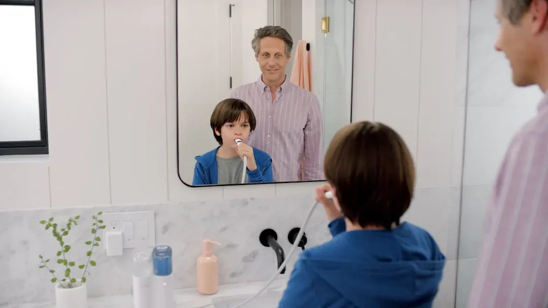 Confident mature man with clear skin and styled hair examining himself in bathroom mirror, demonstrating grooming results fro