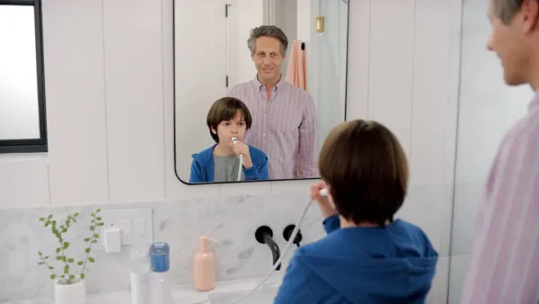 Confident mature man with clear skin and styled hair examining himself in bathroom mirror, demonstrating grooming results fro